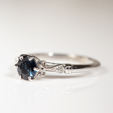 14K white gold vintage-inspired ring featuring a 0.71 carat round blue sapphire with diamond, milgrain, and scrollwork accents.