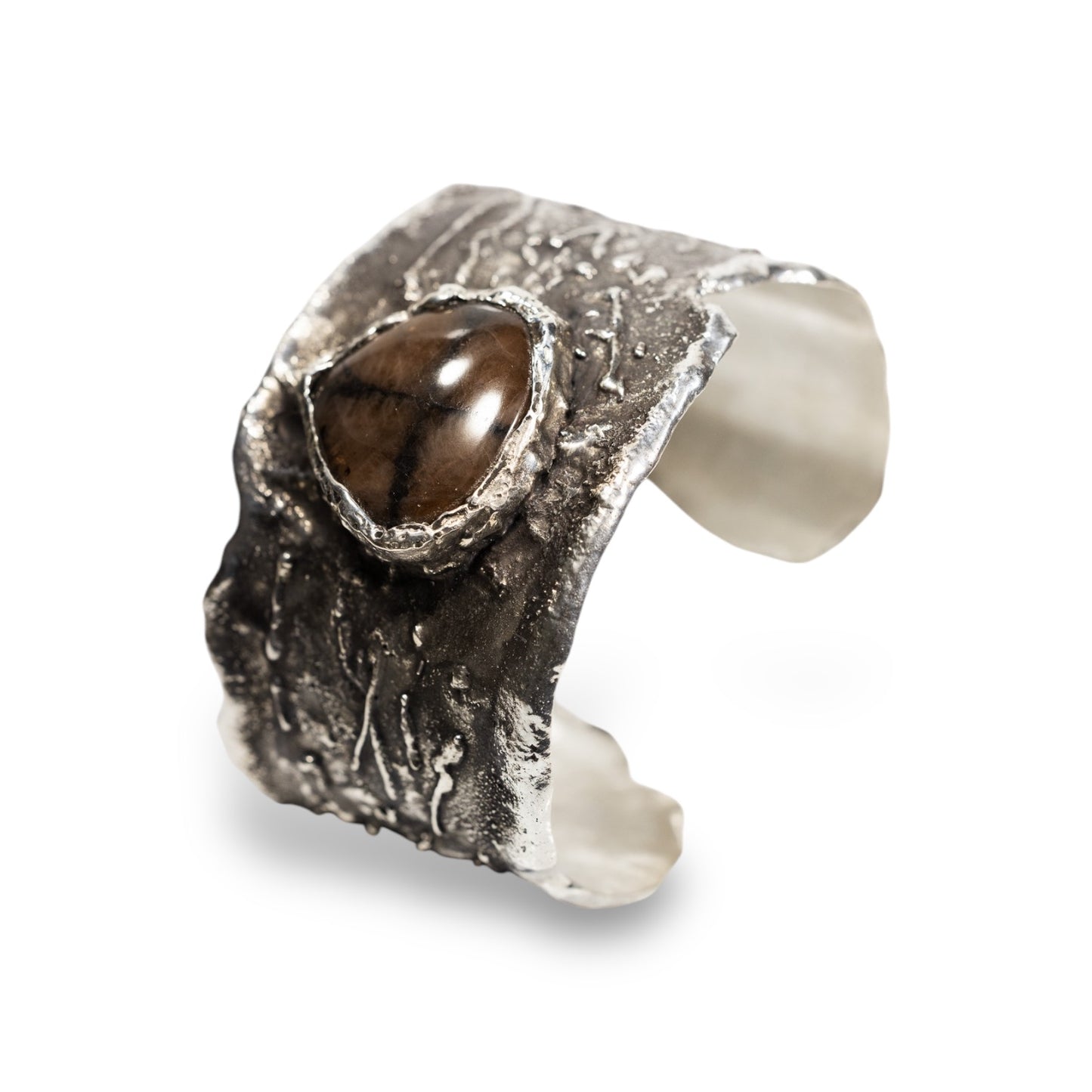 A hand carved sterling silver cuff bracelet with a chiastolite stone centerpiece.