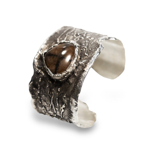 A hand carved sterling silver cuff bracelet with a chiastolite stone centerpiece.