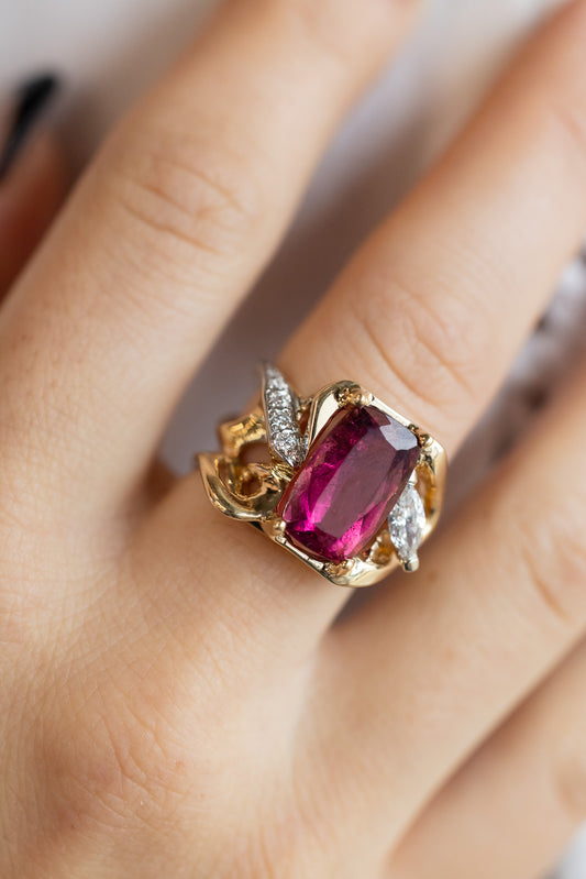 A hand-carved pink tourmaline ring with a yellow gold band, featuring a pink tourmaline on the finger and smaller diamond accents.